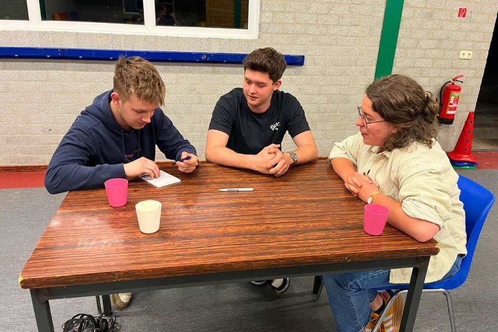 Een groepje leiders zit aan een tafel en werken samen met een opdracht.