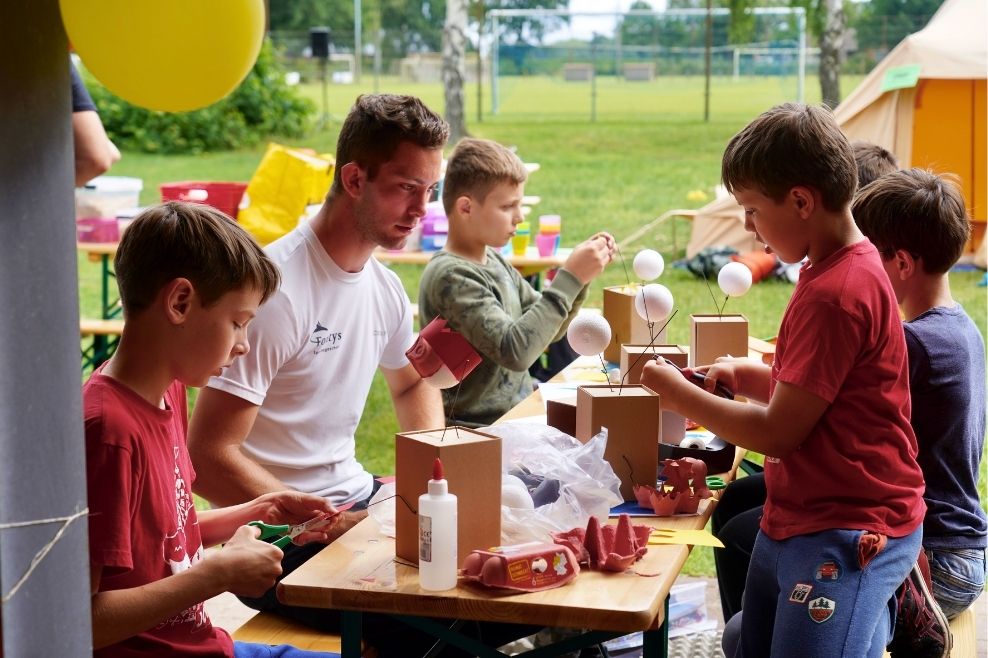 Een groep leden die samen met een leider buiten knutselen tijdens het provinciaal toernooi.
