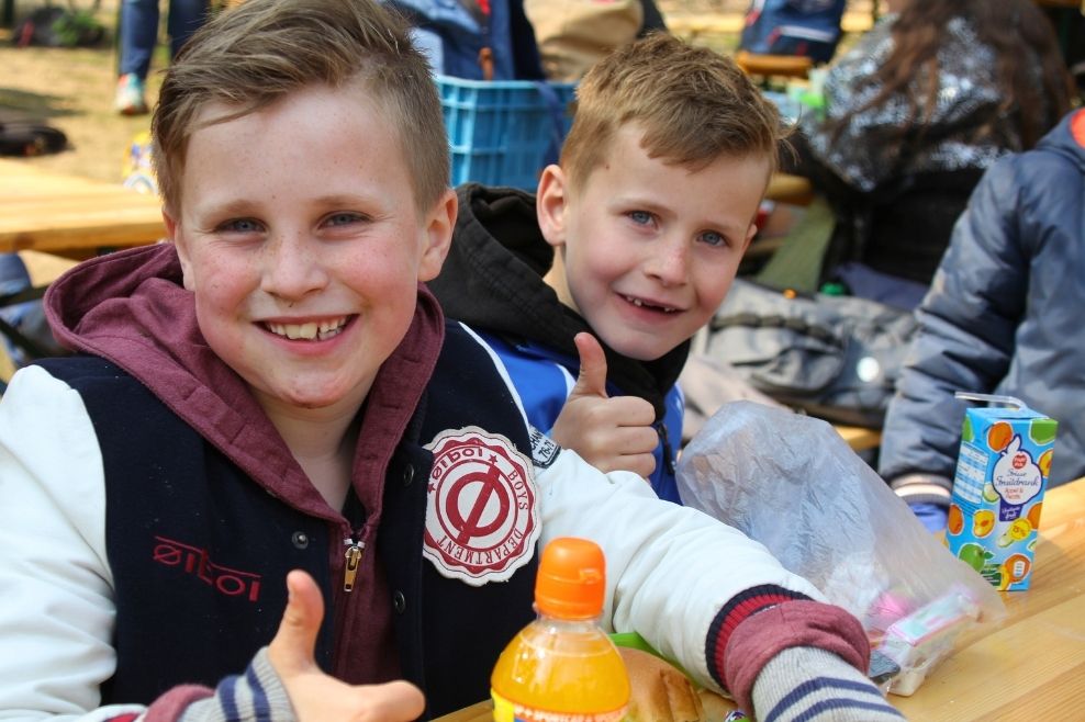 Twee jongens eten een lunch en lachen naar de camera.