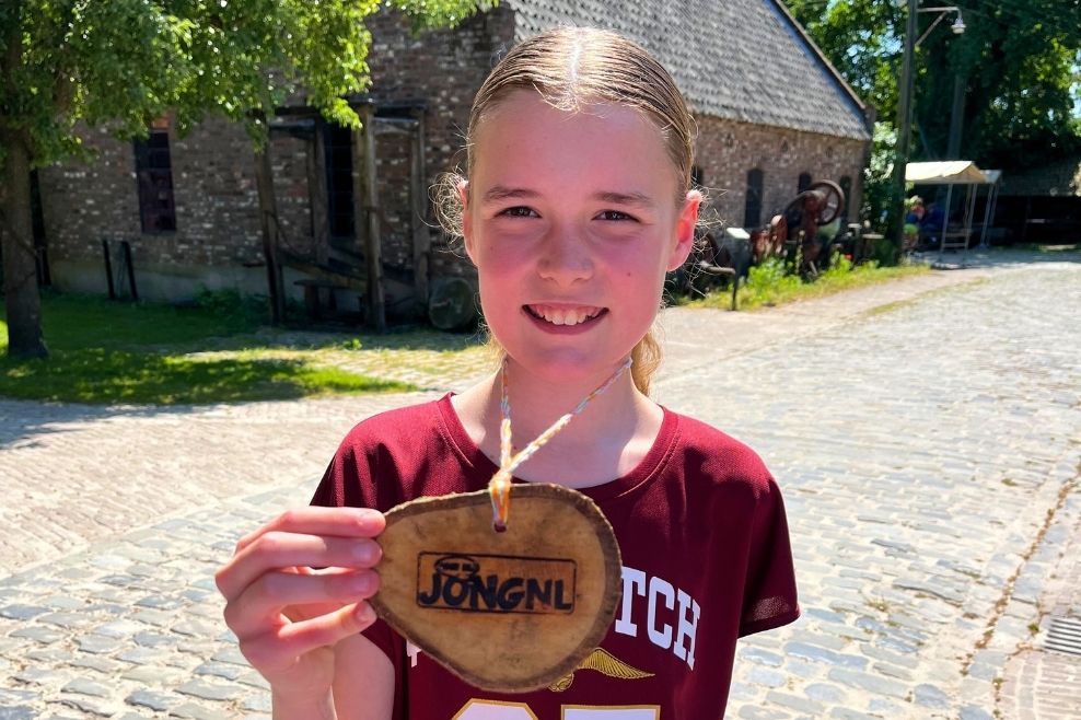 Meisje laat een ketting gemaakt van hout zien met het JongNL logo.