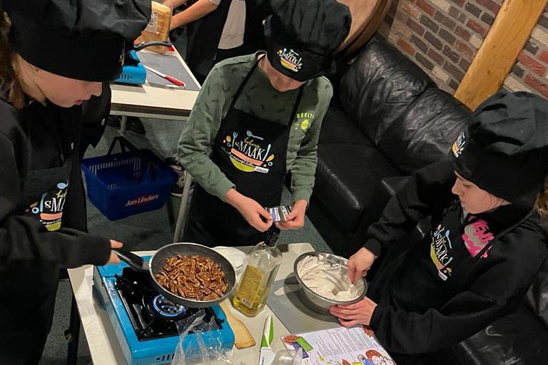 Drie kinderen koken samen een gerecht.