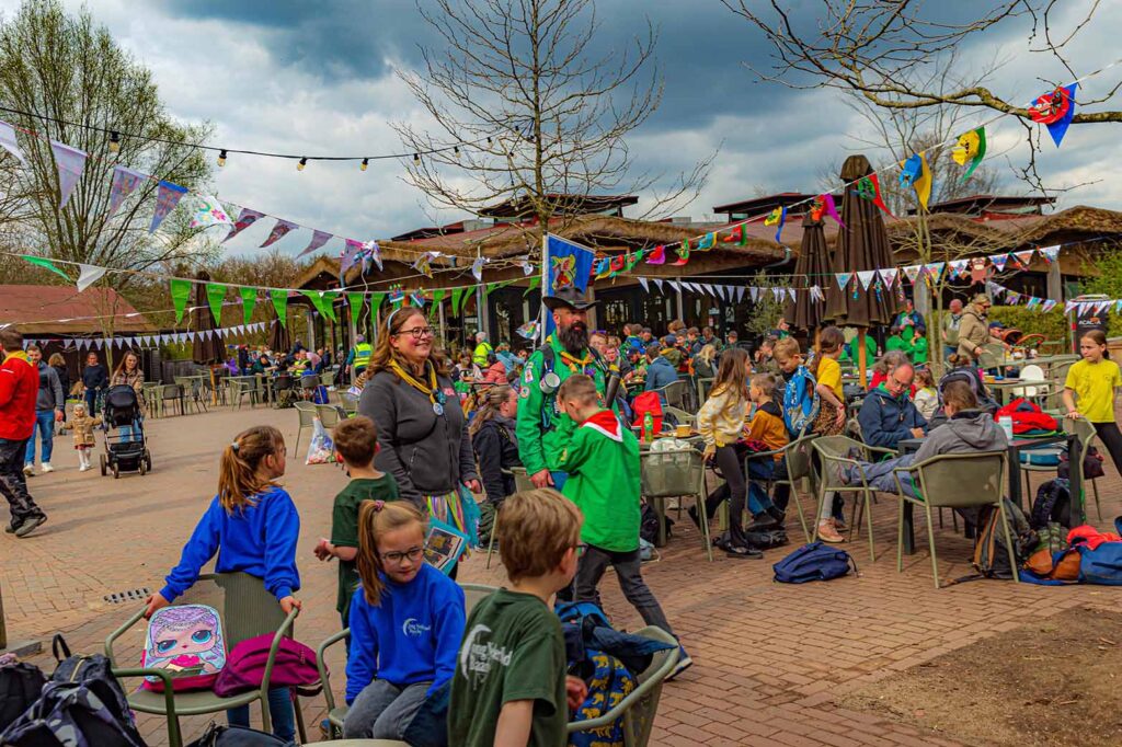 Een grote groep kinderen zit aan tafels en stoelen. De plek is versierd met vlaggetjes.