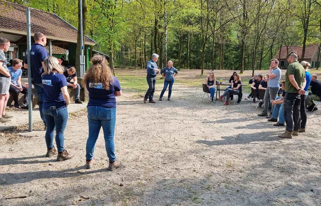 Een grote groep leiders luistert buiten naar de uitleg van een cursusleider.