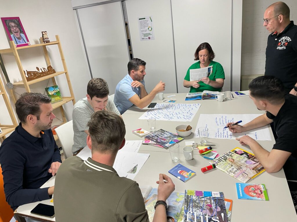 Een groep leiding werkt zit aan een tafel en werkt samen een opdracht uit.