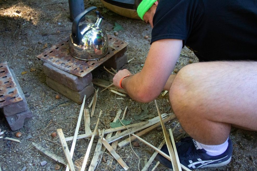 Een leider steekt met kleine houtjes een vuur aan tijdens een outdoorcooking workshop.